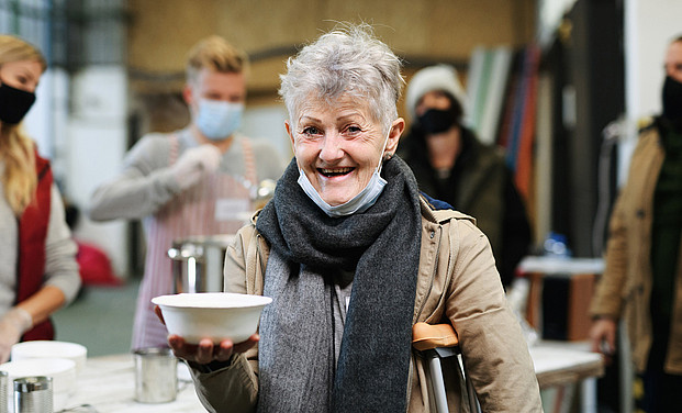 Freiwillige servieren heiße Suppe. Eine ältere Frau hat eine Suppenschüssel in der Hand.