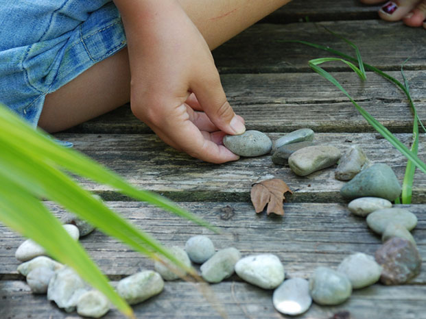 Eine Hand legt besonnen Steine in Form eines Herzens auf Holzdielen am Boden